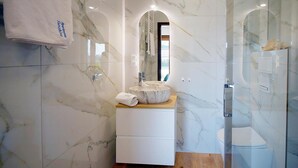 A bathroom with a marble vanity, a sink with a marble countertop, a mirror, and a glass shower enclosure.
