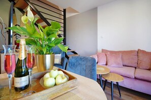 Ein Wohnzimmer mit einer Couch, einem kleinen runden Tisch, einer Holztablett mit Äpfeln und einer Flasche sowie einer Topfpflanze.