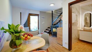 En moderne stue med et spisebord, en trappe og et badeværelse, der ses gennem en åben dør.