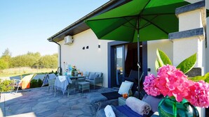 Eine Außenpatio mit Tisch und Stühlen, einem grünen Sonnenschirm und einer Couch mit einem Handtuch.