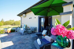 An outdoor patio with a table and chairs, a green umbrella, and a sofa with a towel.