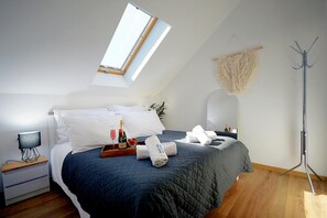 A bedroom with a skylight, a bed with a dark quilt, a bedside table with a lamp, and a floor lamp.