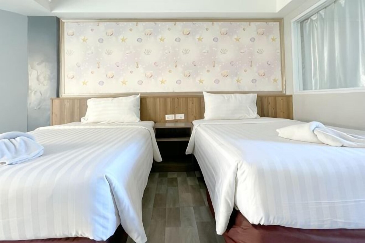 A hotel room with two beds, a wooden headboard, a patterned wall, and a window with curtains.