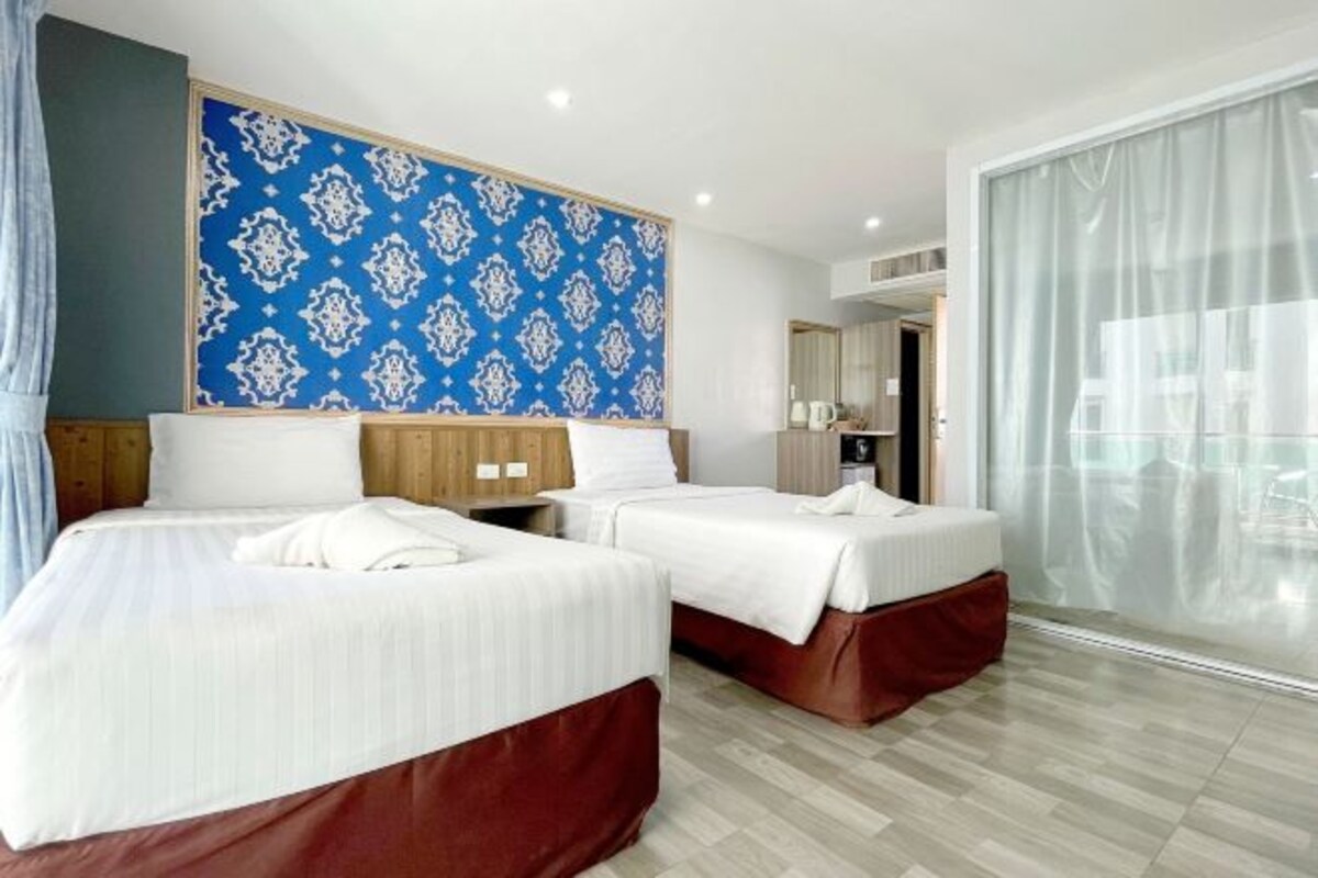 A hotel room with two beds, a large window with curtains, a patterned wall, and a wooden headboard.