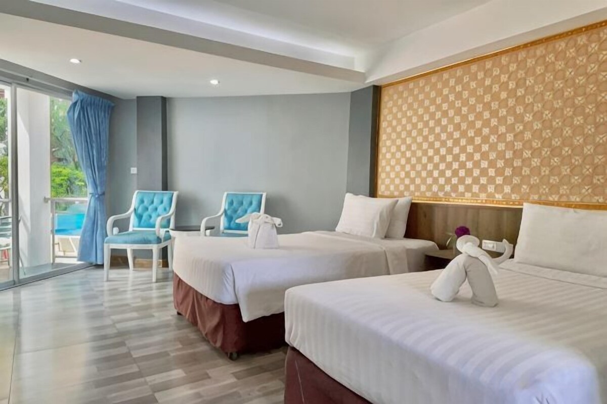 Habitación de hotel con dos camas, una zona de estar con sillas y vistas al exterior.