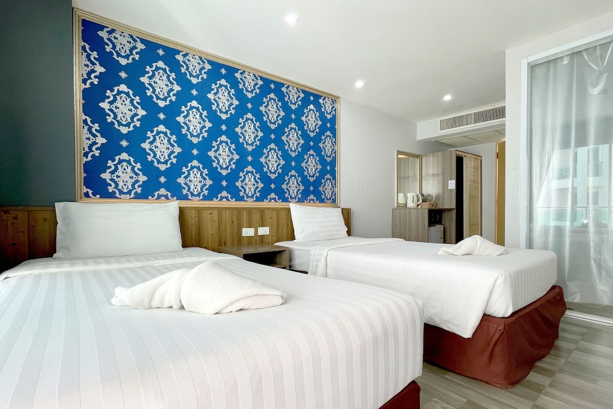 Ein Hotelzimmer mit zwei Betten, einer großen blauen Wand mit Muster, einem Holz-Kopfteil, einem Kleiderschrank und einem Fenster mit Vorhängen.