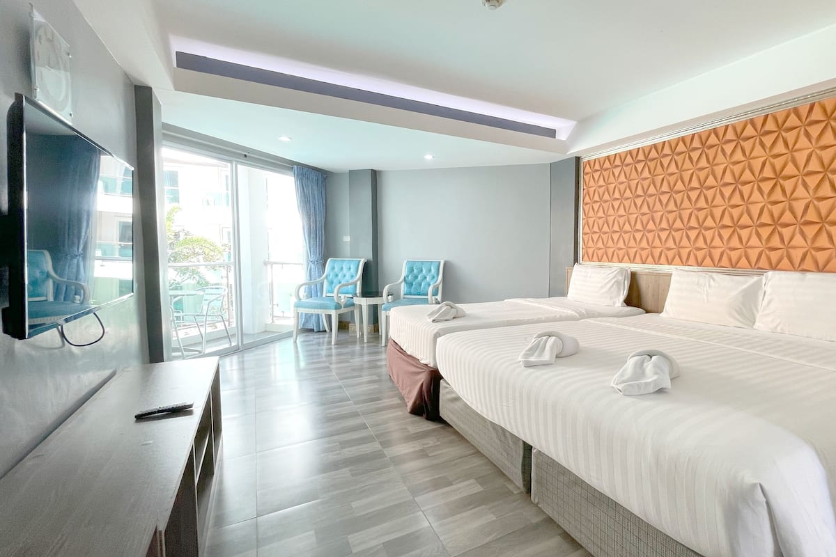 Ein modernes Hotelzimmer mit einem großen Bett, zwei Sesseln, einem Fernseher und einem Balkon mit Blick.