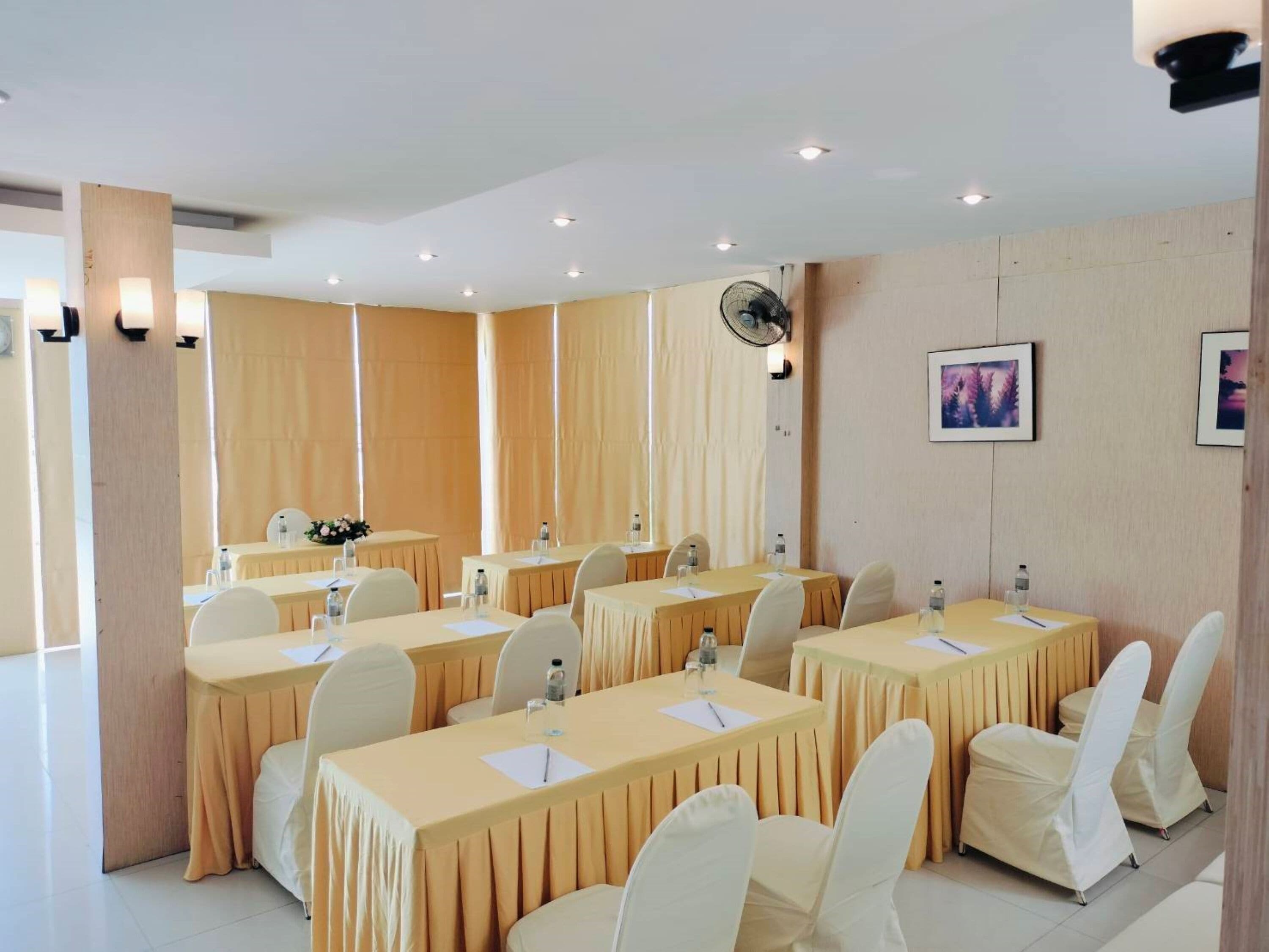 A conference room with multiple tables and chairs, equipped with water bottles and papers, and a fan on the ceiling.