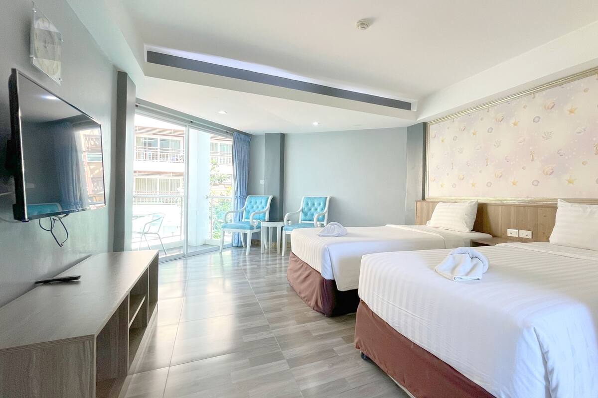 Ein Hotelzimmer mit zwei Betten, einem Fernseher, einem Schreibtisch und einem Sessel.