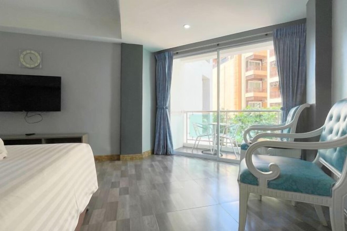 Habitación de hotel con cama, televisión, balcón con una silla y vistas a edificios.