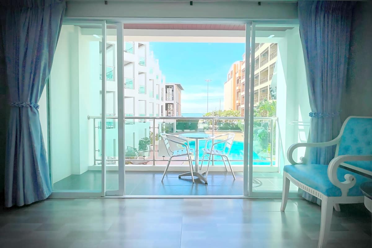 Ein Balkon mit Blick auf einen Swimmingpool und Gebäude, ein weißer Stuhl und eine Glastür.