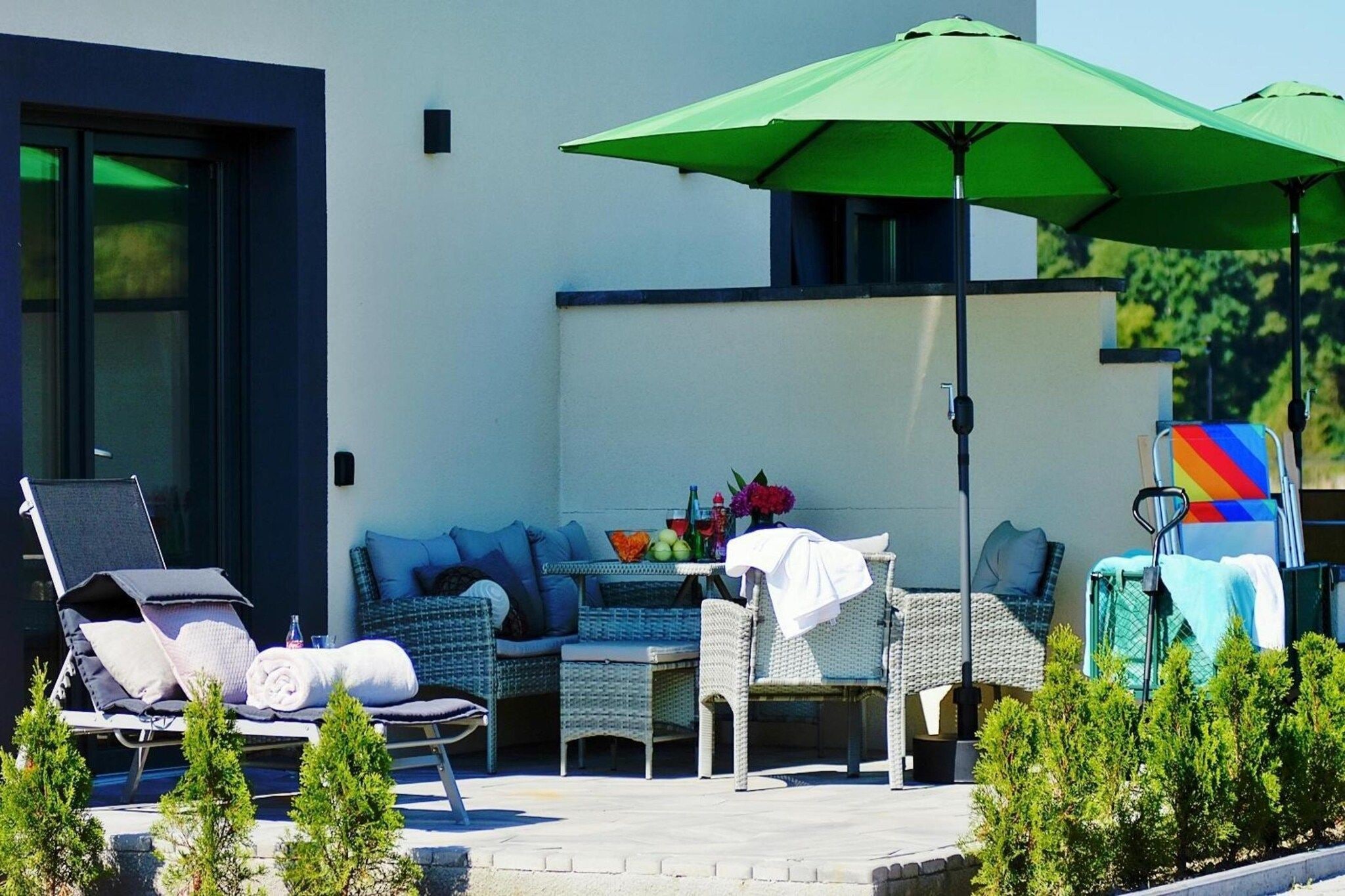 Eine Terrasse mit Gartenmöbeln, darunter Liegestühle und eine Sitzecke, unter einem grünen Sonnenschirm.