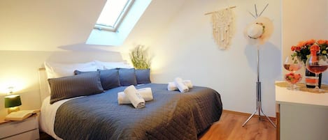 A bedroom with a skylight, a bed with a dark quilt, a bedside table with a lamp, and a nightstand.