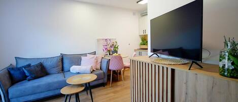 A modern living room with a sofa, a coffee table, a TV, and a small dining area.