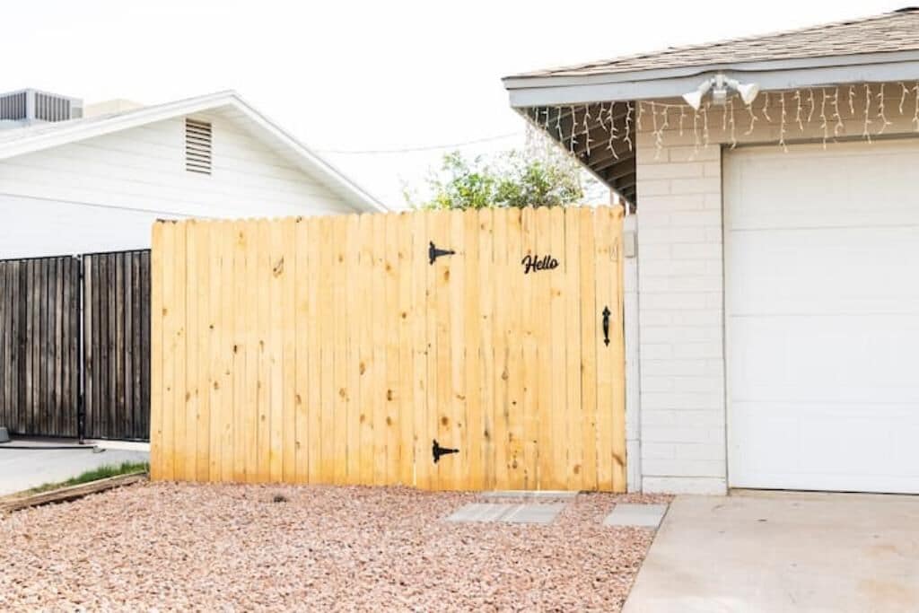 A wooden fence with a "Hello" sign, a garage door, and a gravel driveway.