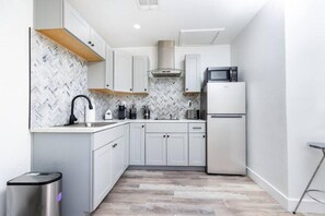 A modern kitchen with white cabinets, a herringbone-patterned backsplash, a stainless steel trash bin, and a compact refrigerator. - Stylish & Modern Studio in Phoenix ~ QueenBed (Phoenix)