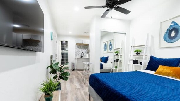 Una camera da letto moderna con un letto grande, una ventola a soffitto, una TV a parete e un angolo cottura sullo sfondo.