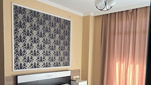 A modern hotel room with a large bed, a headboard with a decorative panel, a nightstand, and a large window with curtains. - Mahali Hotel (Batumi)