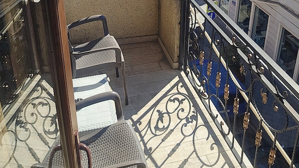 A balcony with a wrought iron gate, two chairs, and a view of the cityscape. - Mahali Hotel (Batumi)