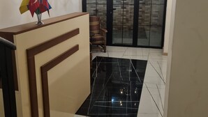 A spacious room with a black and white tiled floor, a wooden reception desk, a chandelier, and a view through a glass door to a tiled area. - Mahali Hotel (Batumi)