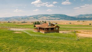 Eine Holzhütte mit Veranda, umgeben von einem eingezäunten Grundstück und einem Bergpanorama.