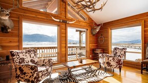 Eine Holzhütte mit großen Fenstern, Ledersesseln und Geweihen an den Wänden.