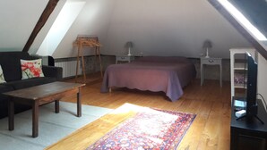 Un acogedor dormitorio en el ático con una cama, una mesa de madera, una silla, una lámpara y un televisor.