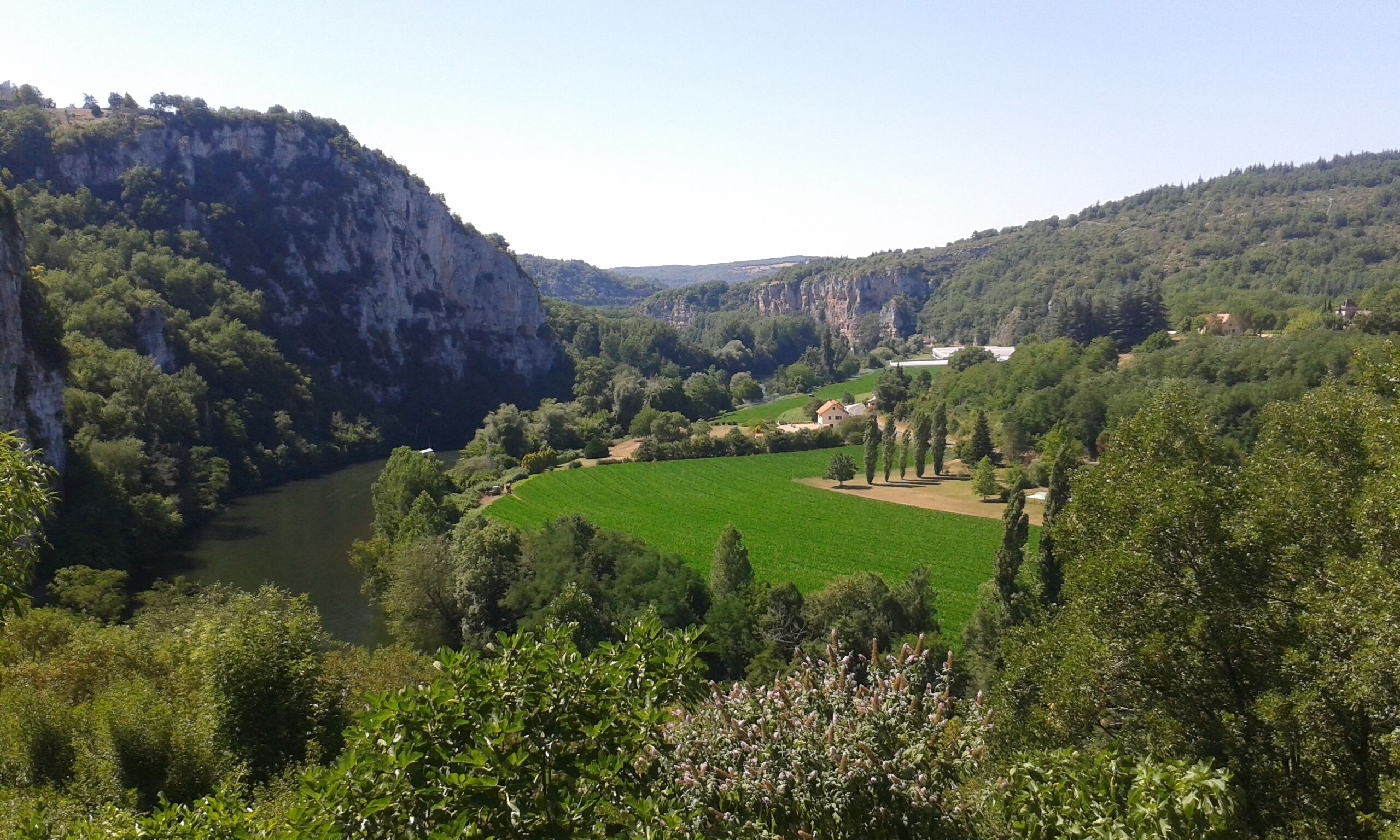 A valley with a river, green fields, and a house with a view of the river and hills.