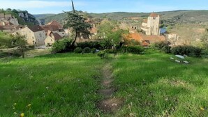 Un pueblo rural con edificios de piedra, una iglesia y un sendero que atraviesa la vegetación.