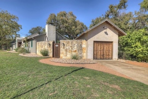 A residential property with a stone facade, a wooden garage door, and a well-maintained lawn. - 406 Lodge-a: Hot-tub & 2 Blks to Main St (Fredericksburg)