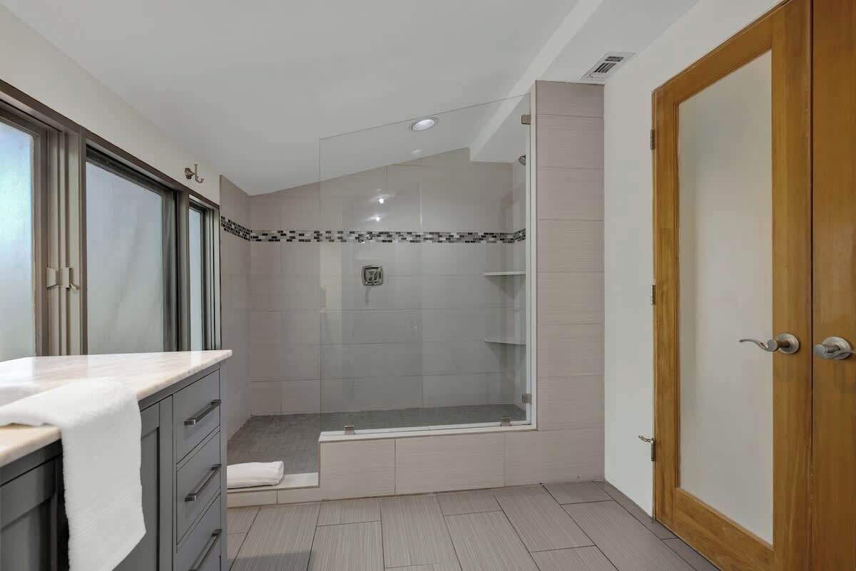 Un baño moderno con ducha de vidrio, tocador con una toalla y puerta de madera.