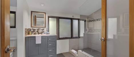 Une salle de bain moderne avec un meuble-lavabo gris, un grand miroir et une douche à parois de verre.