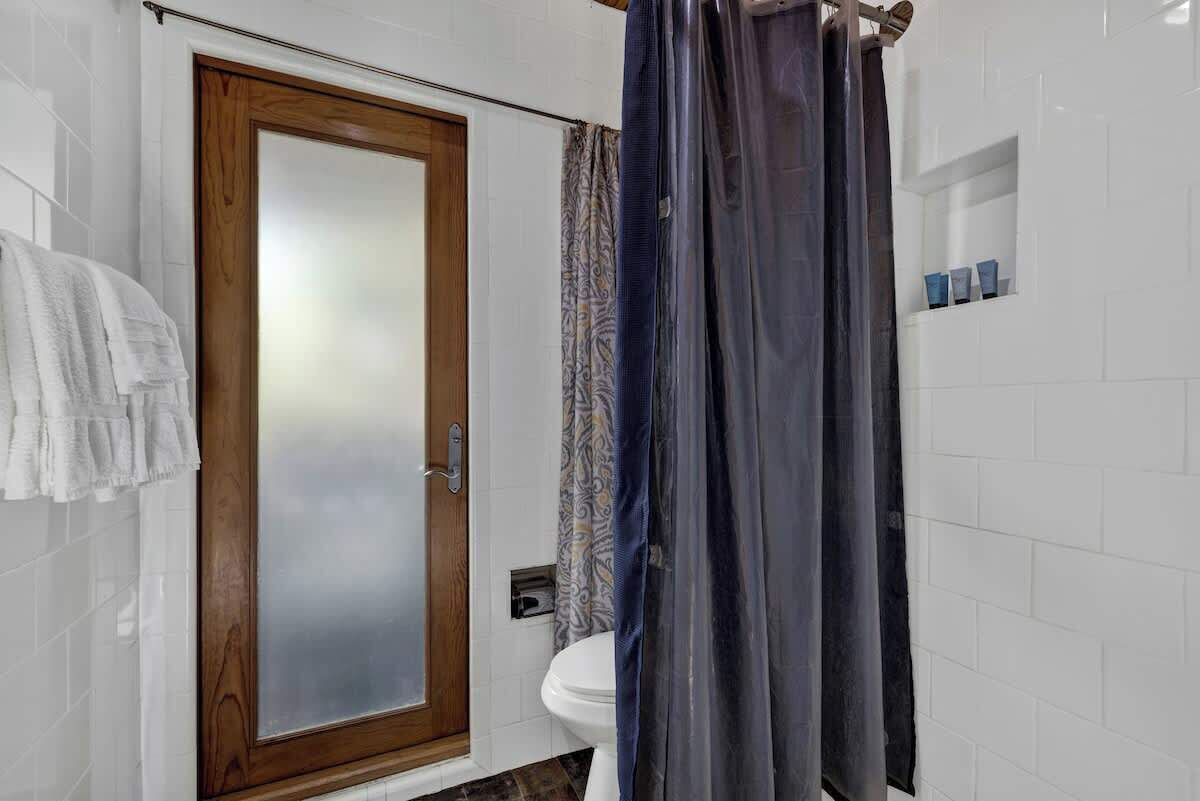 A bathroom with a wooden door, a toilet, a shower curtain, and a towel rack.