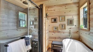 Une salle de bain rustique, avec des murs en bois, une douche en verre, une baignoire blanche et un lavabo.