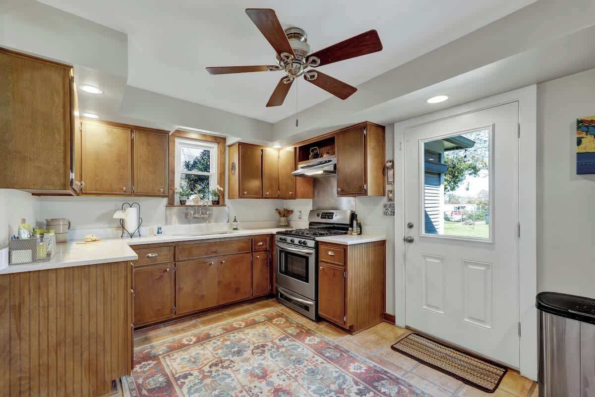 Une cuisine avec des armoires en bois, une cuisinière et un ventilateur de plafond.