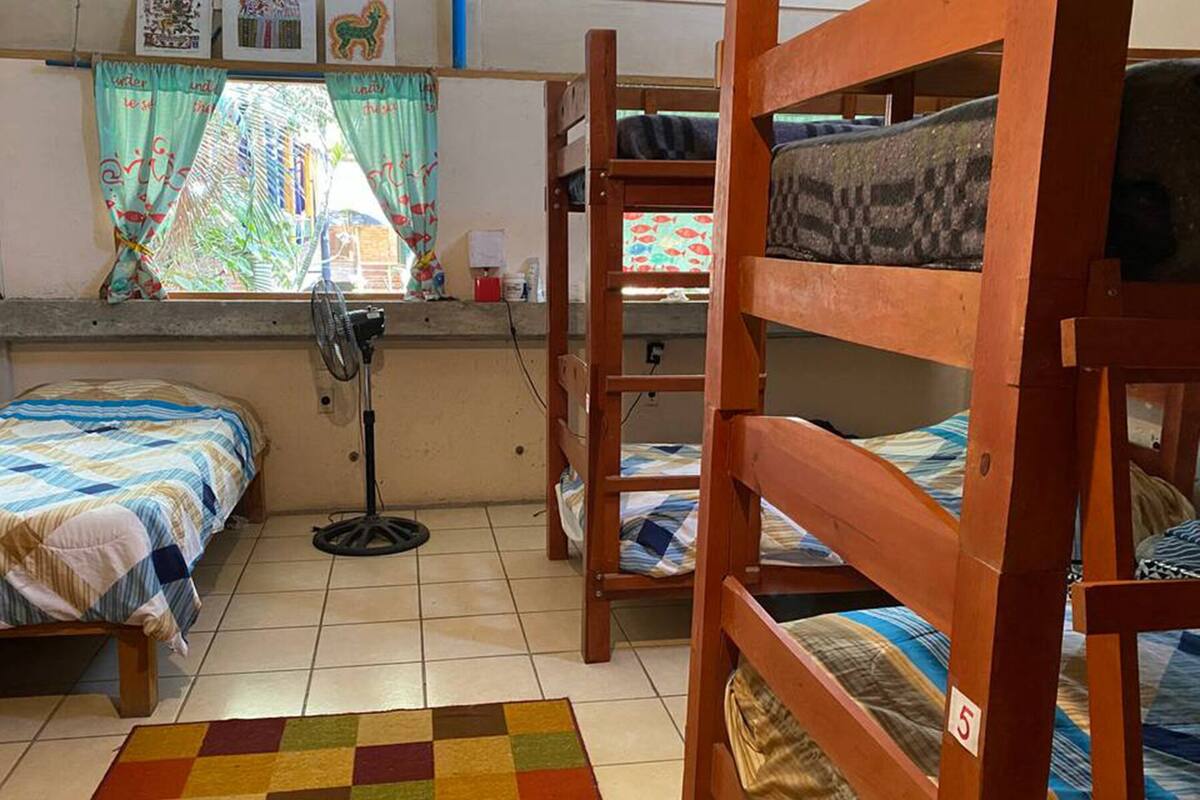 A dormitory room with bunk beds, a fan, a window with curtains, and a tiled floor.