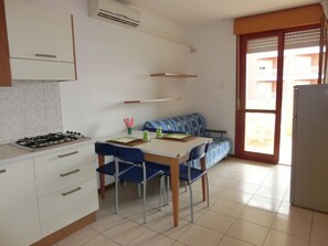 Una cocina compacta con estufa a gas, una mesa de comedor con sillas, un sofá y un refrigerador.