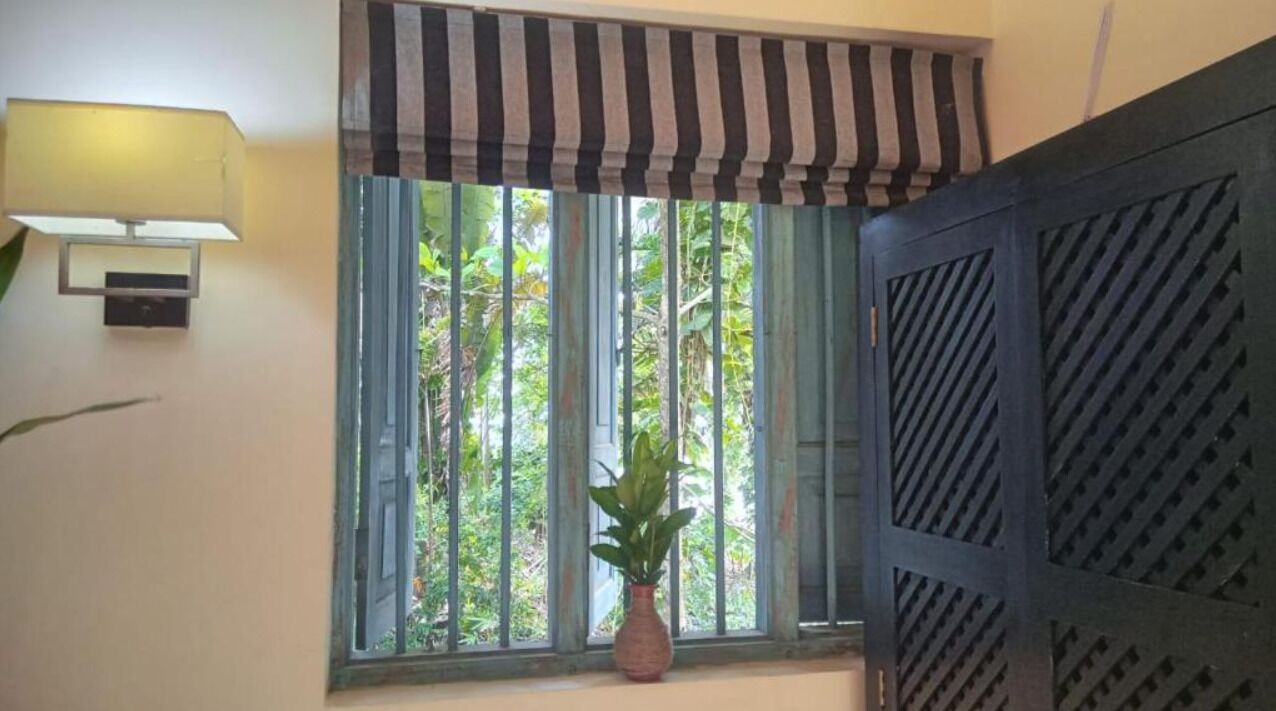Ein Zimmer mit Fenster, einer Topfpflanze und einer Wandlampe.