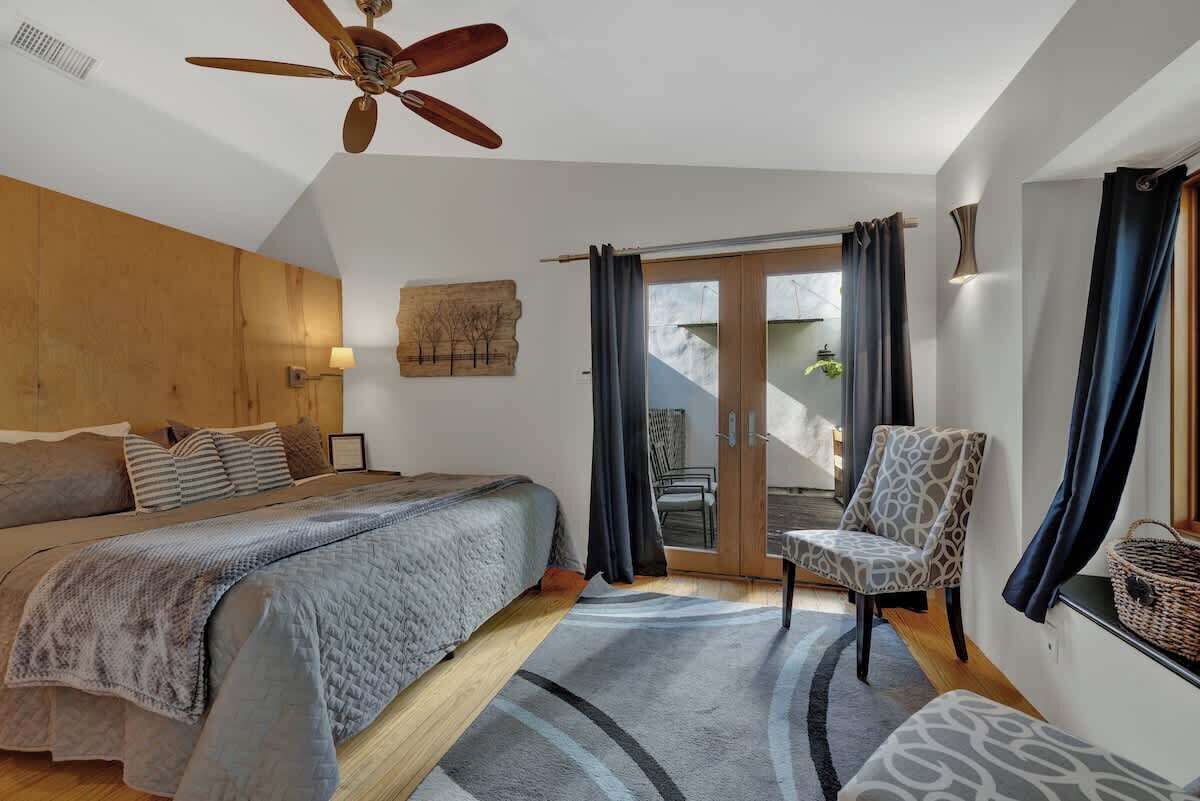Une chambre avec un lit, une chaise, un ventilateur de plafond et une vue sur l’extérieur.