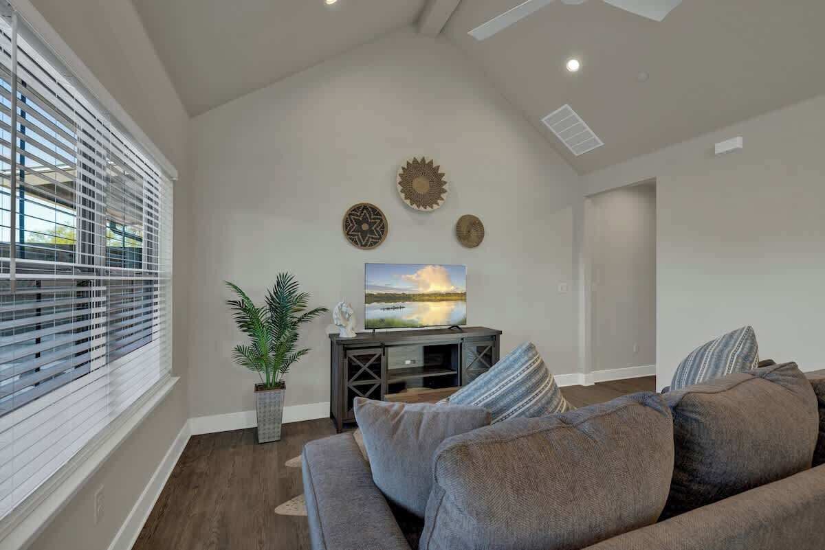 A living room with a gray sofa, a TV on a wooden stand, decorative wall art, and a potted plant.