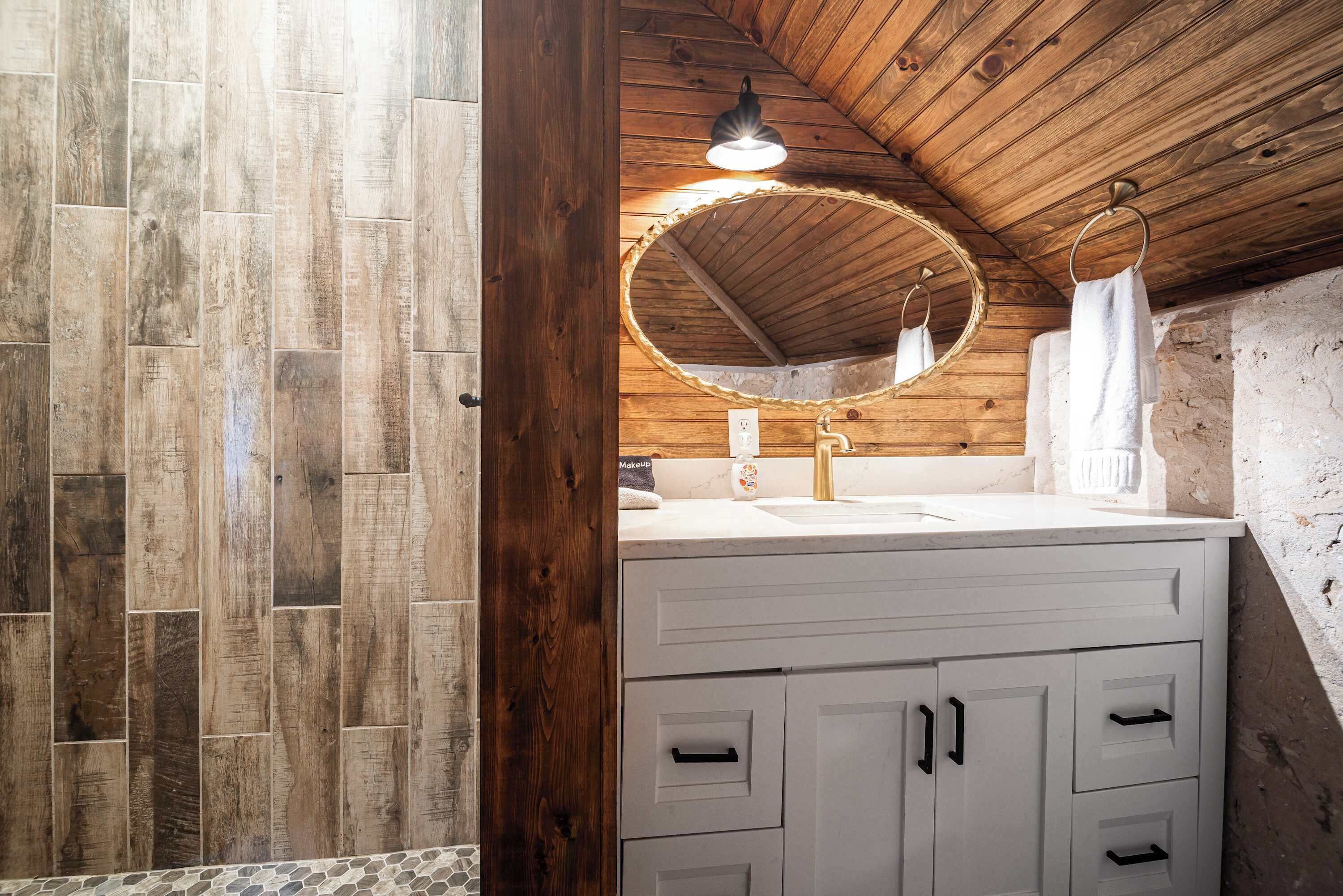 A bathroom with a wooden ceiling, a round mirror, a sink, and a towel rack.