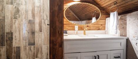 A bathroom with a wooden ceiling, a round mirror, a sink, and a towel rack.