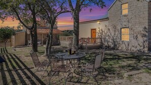 A stone building with a porch, a fenced yard, and a table with chairs.