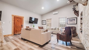 A living room with a beige sofa, a brown armchair, and a television on the wall.