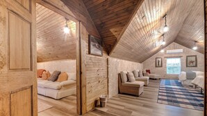 A spacious loft with wooden walls and a high ceiling. It features a large open living area with a sofa set, a wicker chair, and a patterned rug.