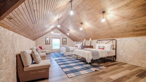 A cozy attic bedroom with a sloped ceiling, a bed, a sofa, and a window.