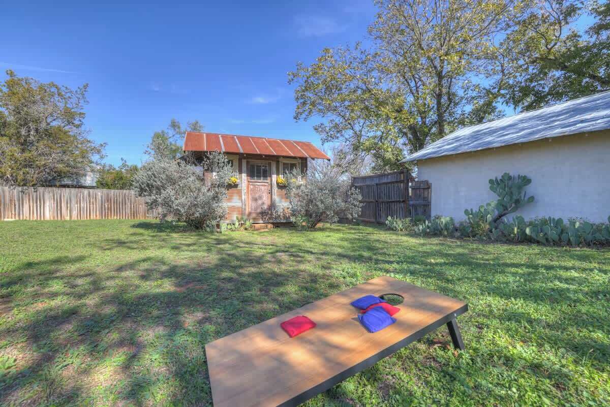 A wooden picnic table with cushions in a backyard with a house and cacti.