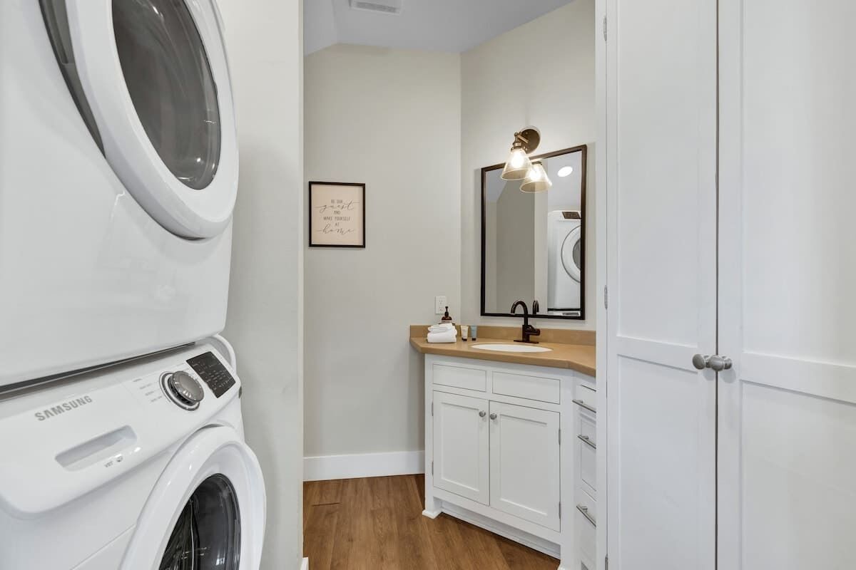 A laundry room with a Samsung washing machine, a sink, and a mirror with a light fixture.