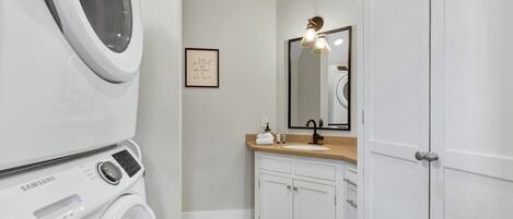 A laundry room with a Samsung washing machine, a sink, and a mirror with a light fixture.