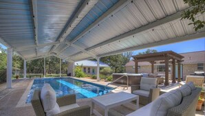 Zona de piscina exterior techada con mobiliario de descanso, un jacuzzi y una pérgola.